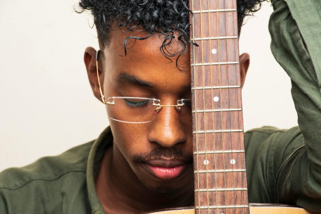 A young man with glasses holding a guitar, emphasizing creativity and music passion.
